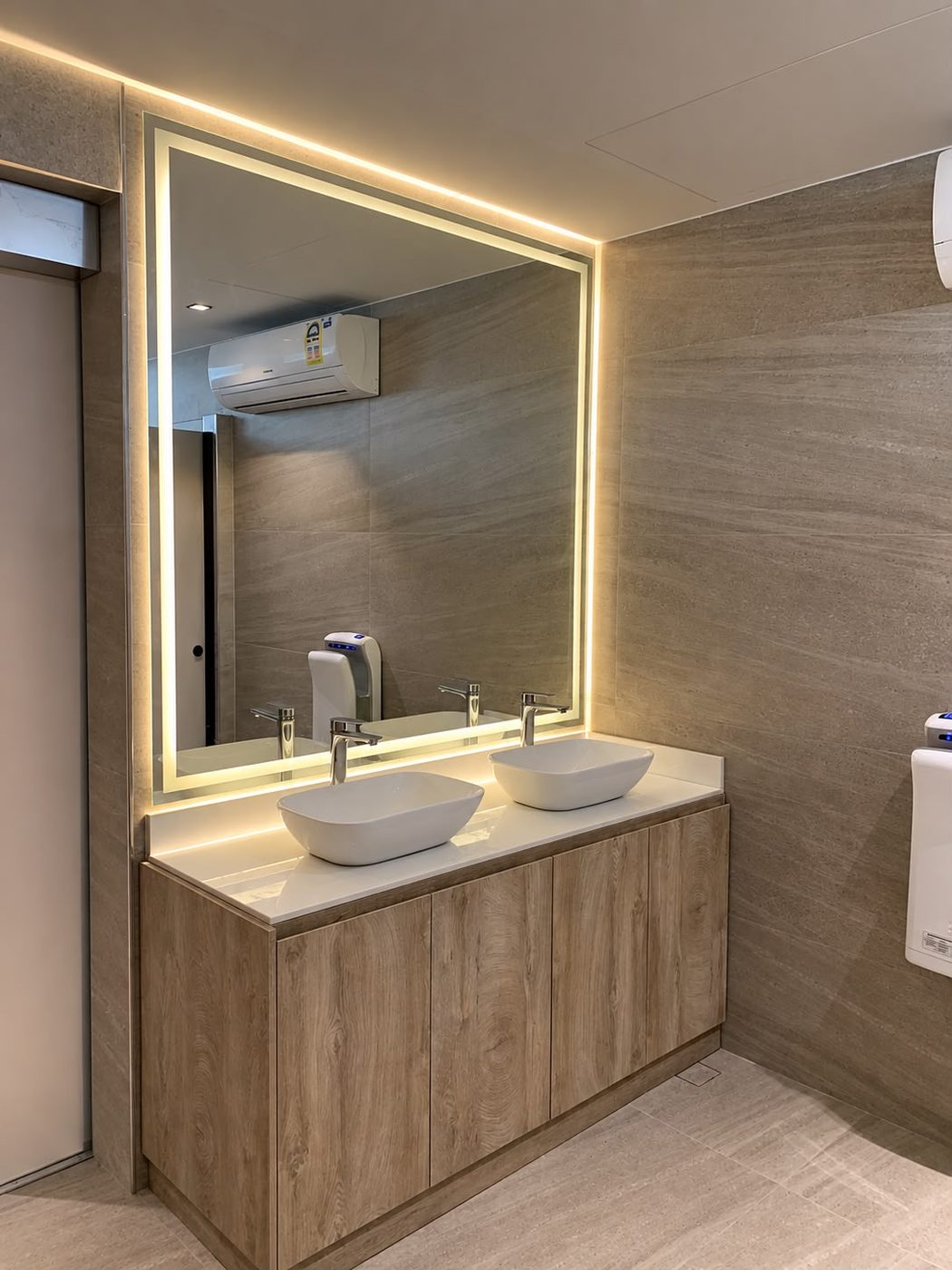 Light oak double vanity with twin vessel basins and a large backlit mirror